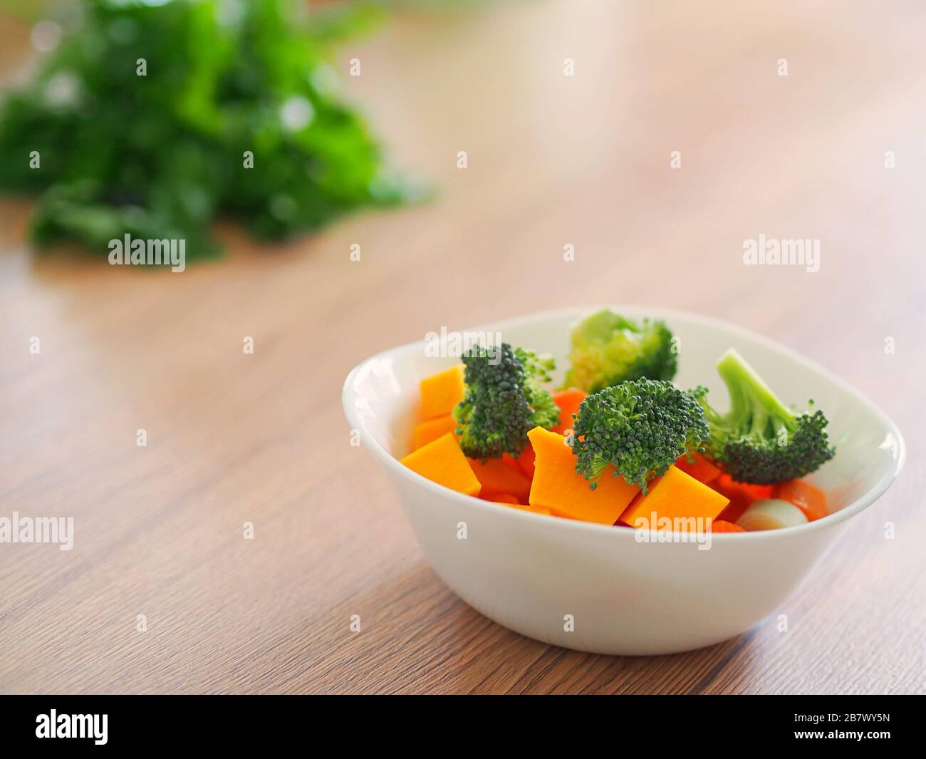 Nahaufnahme einer Tasse mit frischem Gemüse, darunter Karotte und Brokkoli auf einem Holzküchentisch mit Petersilie im Hintergrund. Stockfoto