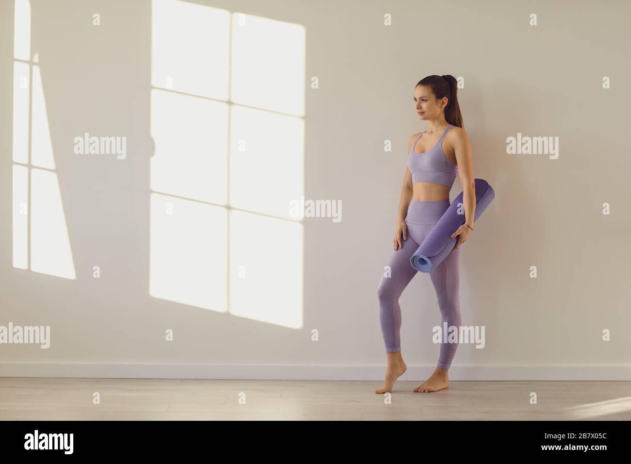Yoga-Frau. Fröhliche Sportfrau mit Yogamatte an weißer Wand in einem hellen Raum. Stockfoto