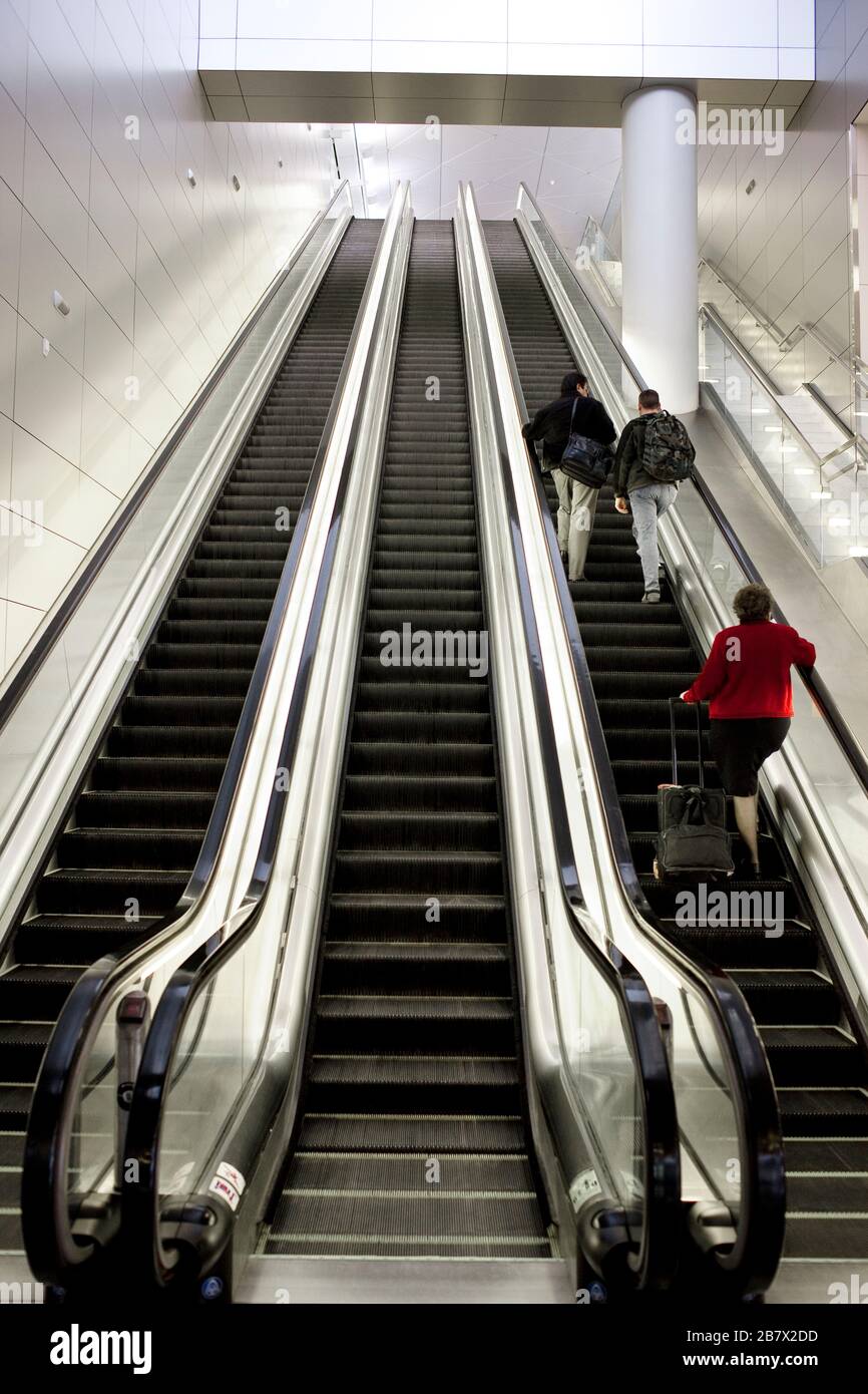 Reisende und ihr Gepäck fahren die Rolltreppe an einem Flughafen hoch. Stockfoto