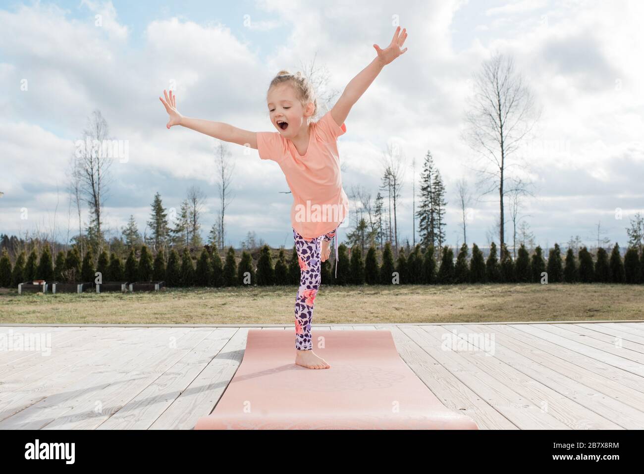 Junges Mädchen balanciert auf einer Yogamatte in ihrem Hinterhof zu Hause Stockfoto