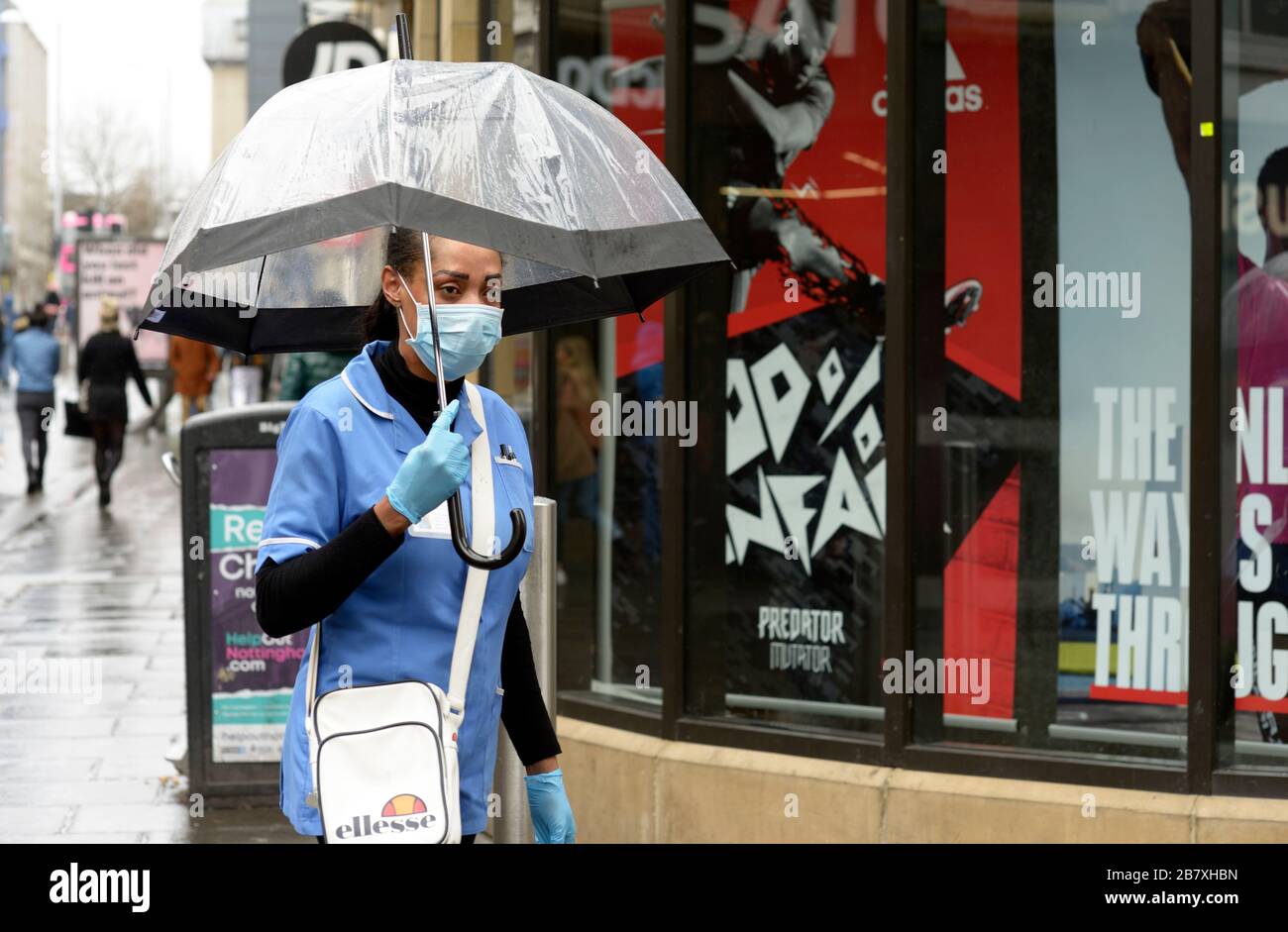 Gesundheitsarbeiter, in Uniform mit Maske und Handschuhen, auf dem Weg zum Geldautomaten im Regen, während des Corona-Virus-Ausbruchs. Stockfoto