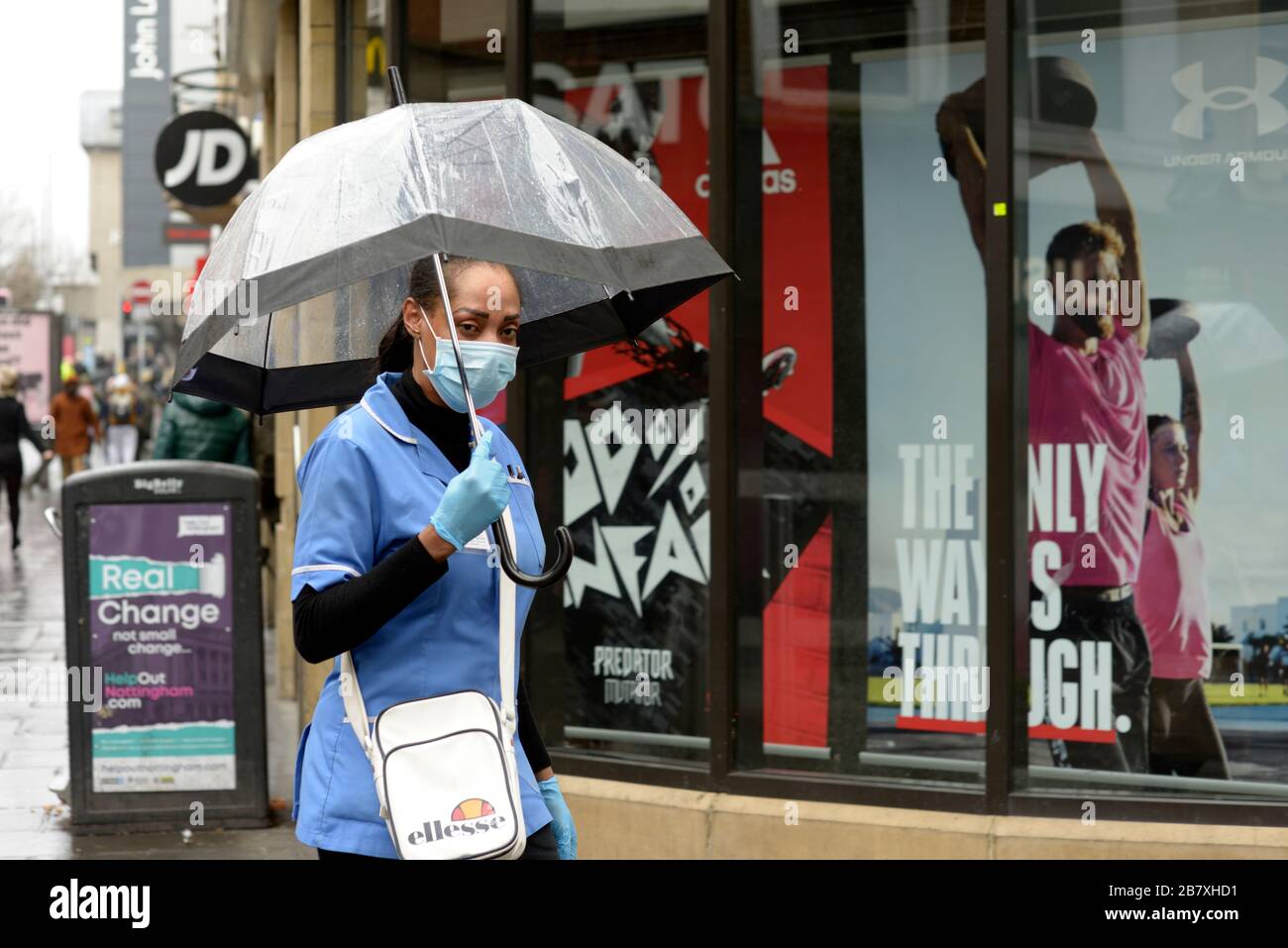 Gesundheitsarbeiter, in Uniform mit Maske und Handschuhen, auf dem Weg zum Geldautomaten im Regen, während des Corona-Virus-Ausbruchs. Stockfoto