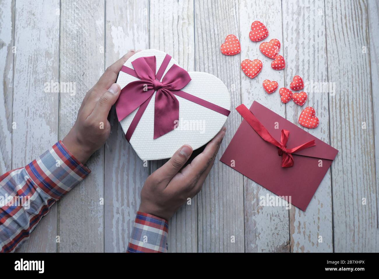 Mann's Hand hält Herz Form Geschenk und Umschlag auf dem Tisch Stockfoto