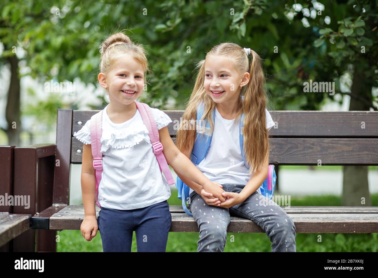 Zwei kleine Kinder lachen und plaudern auf einer Bank. Das Konzept geht zurück auf Schule, Familie, Freundschaft und Kindheit. Stockfoto