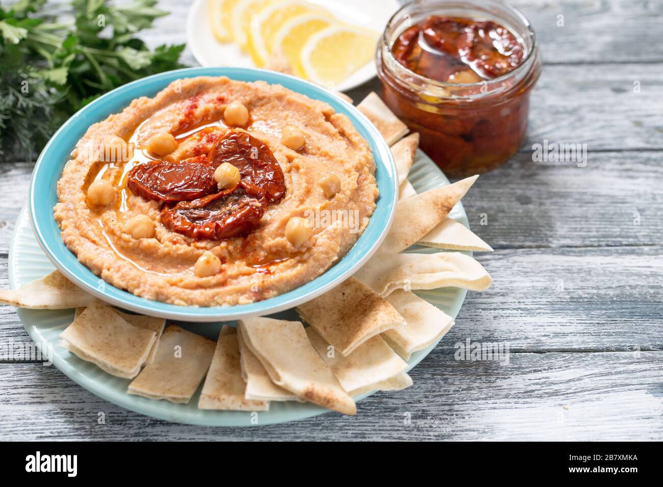 Eine Schüssel cremig hausgemachter Hummus mit sonnengetrockneten Tomaten, Olivenöl und Pita Pommes. Traditionelle vegane gesunde Mahlzeit Stockfoto