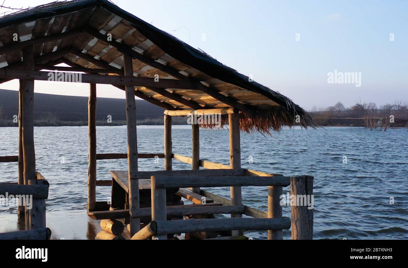 Ein Pavillon aus Holz schwimmt auf einem Fluss. Sonnenuntergang am See. Ein Haus am Wasser. Ein Grillplatz am Ufer des Flusses. Picknickplatz Stockfoto