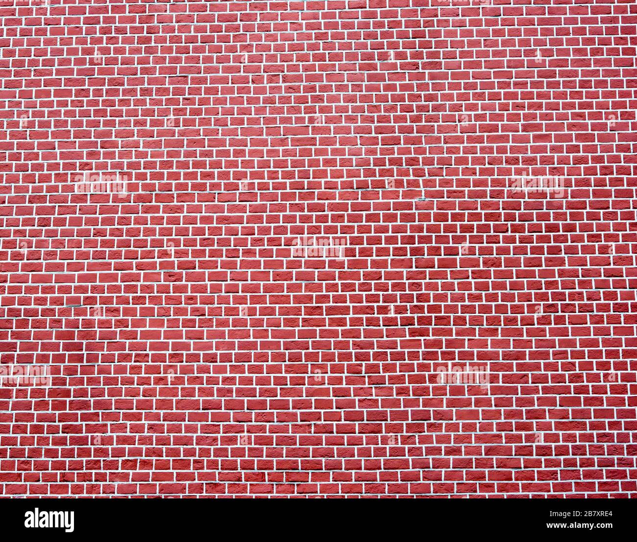 Eine glatte Ziegelwand in kalter rot-brauner Farbe mit weißen Gelenken. Strukturierter Hintergrund. Stockfoto