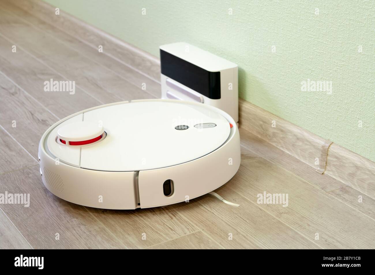 Roboter-Staubsauger auf Laminatfußboden wird von der Basisstation geladen. Intelligente Reinigungstechnologie. Stockfoto