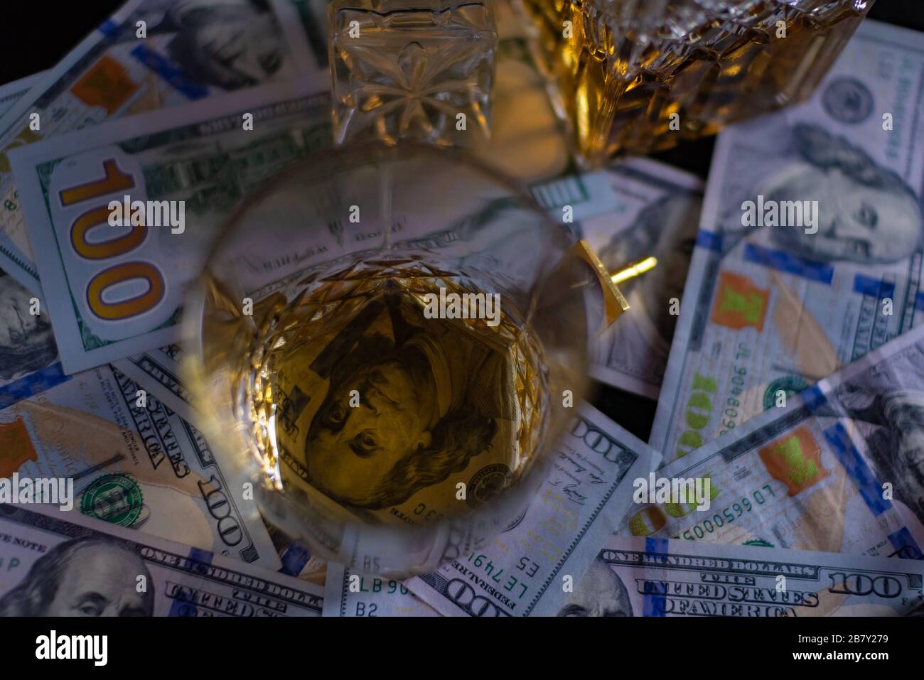 Dollar-Geld auf dem Tisch. Die 100-Dollar-Rechnung scheint durch den transparenten Boden eines Glases Whisky Stockfoto