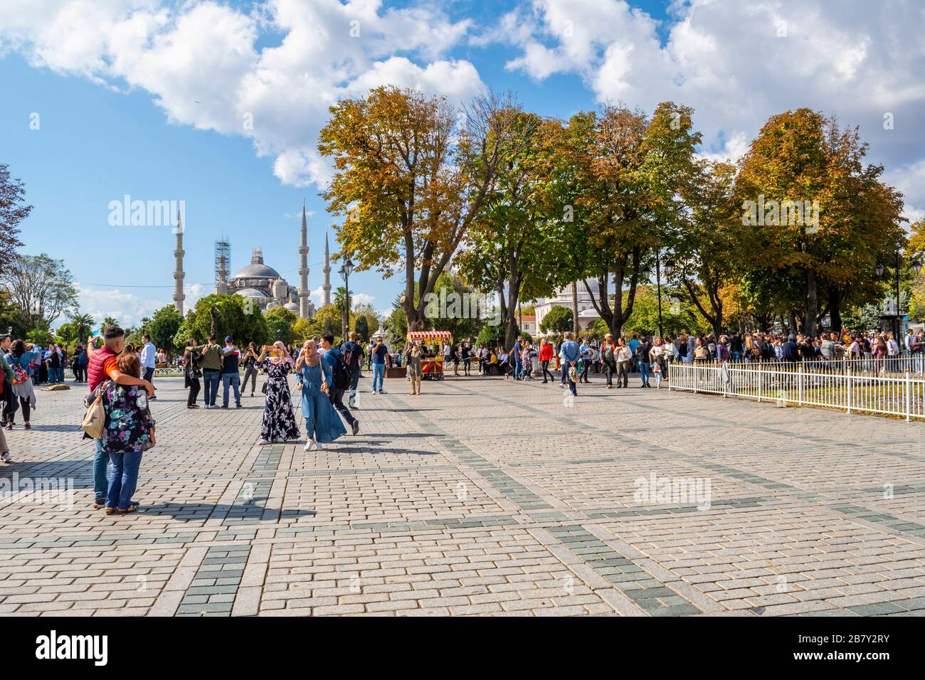 Westliche und muslimische Touristen und einheimische Türken genießen einen sonnigen Tag auf dem Sultanahmet-Platz mit der Blauen Moschee in der Ferne. Stockfoto