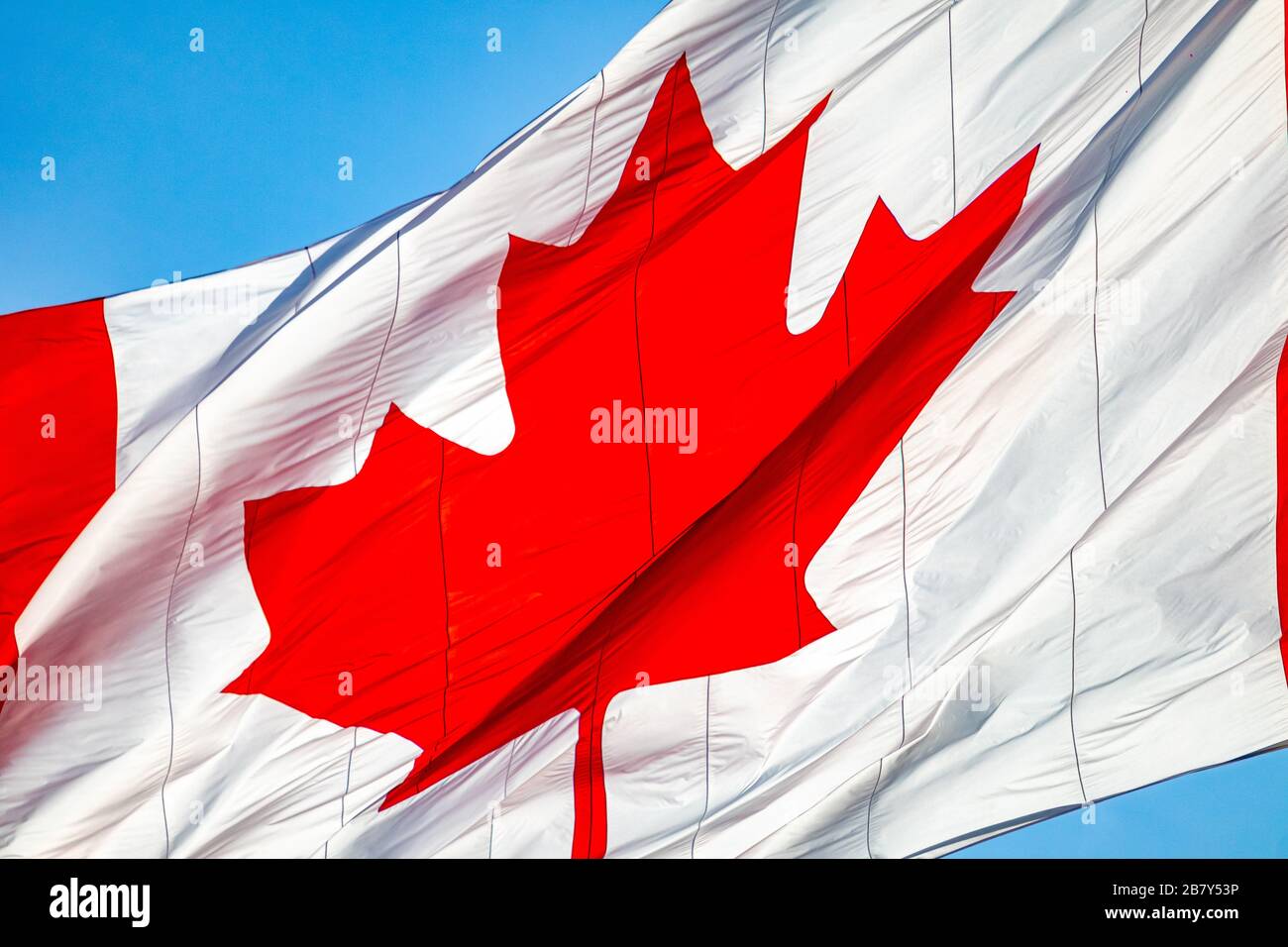 Eine Nahansicht einer großen kanadischen Flagge zeigt das berühmte rote Ahorn-Blattsymbol auf weißem Grund und schippelt, während es im Wind weht. Stockfoto
