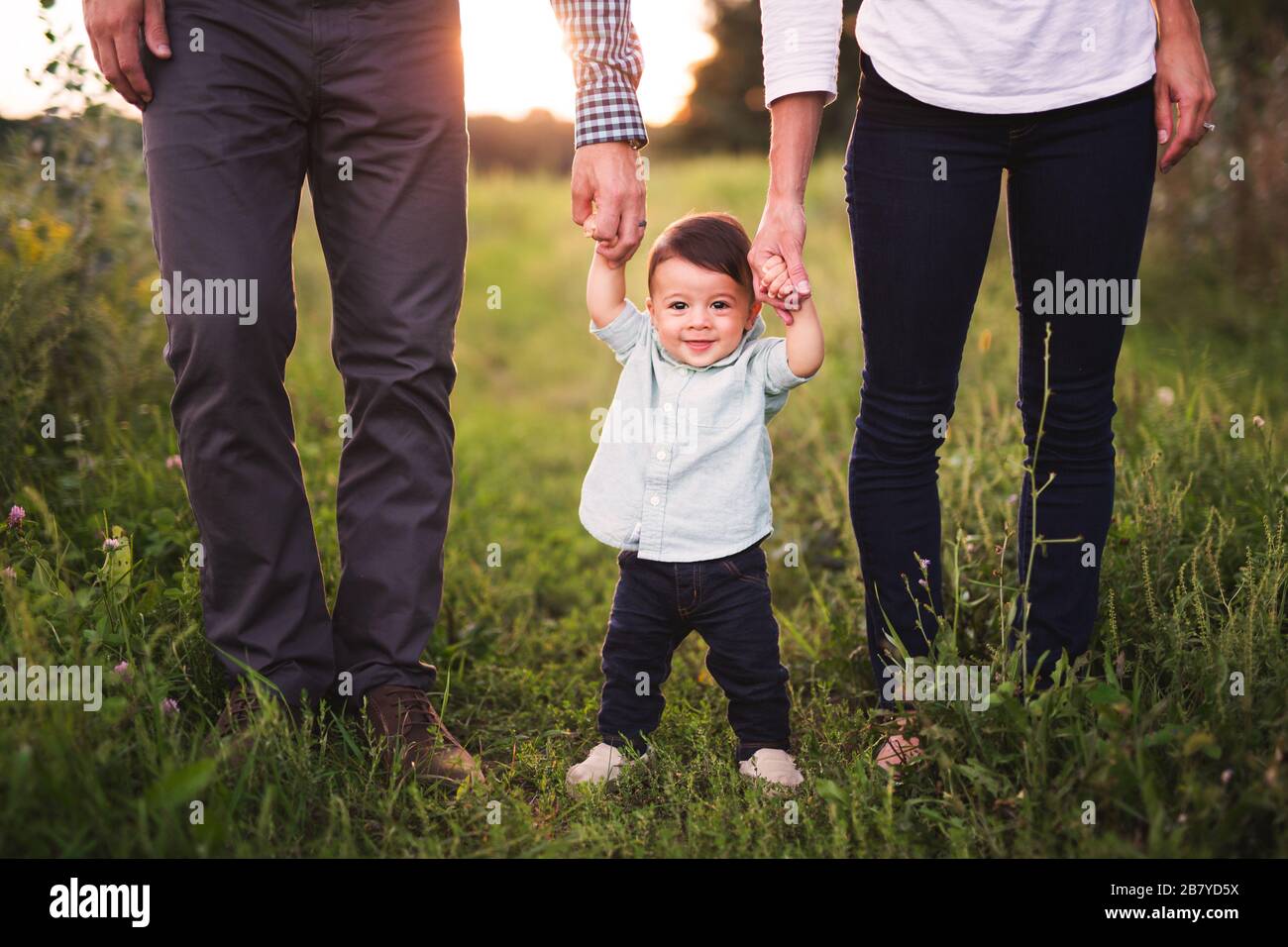 Niedlicher kleiner Junge, der die Hände seiner Eltern hält Stockfoto