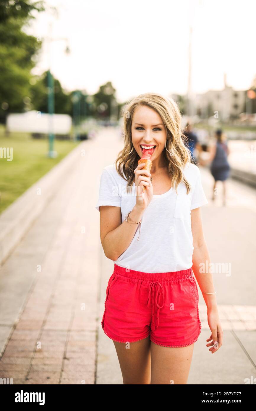 Junge Frau leckt einen Eiskegel, während sie am Sommerabend spazieren geht Stockfoto