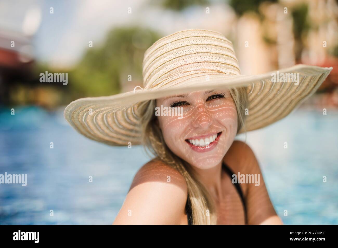Lächelnde junge Frau, die im tropischen Pool mit Sonnenhut baden kann Stockfoto