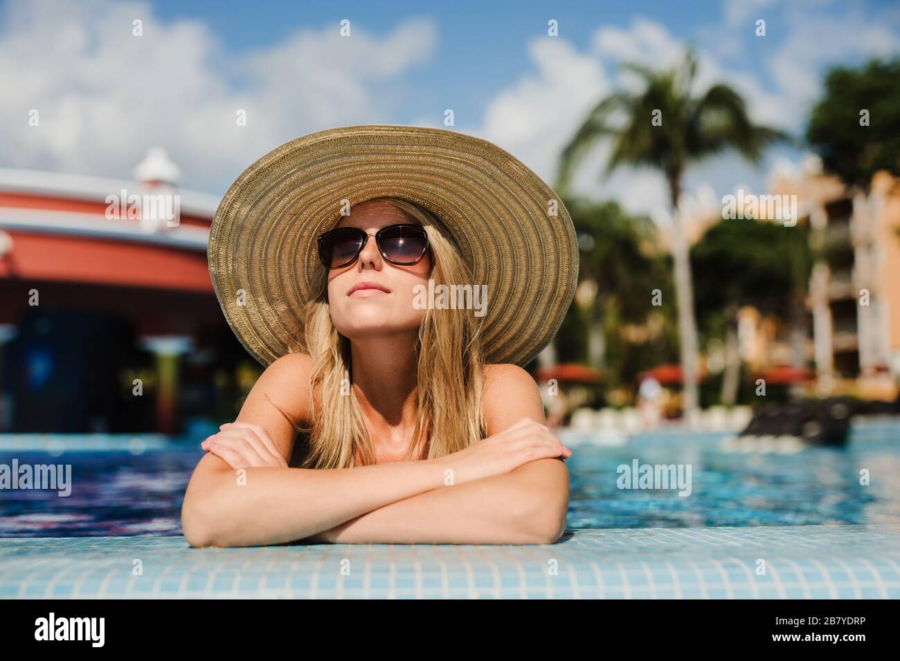 Junge Frau, Sonnenbaden im tropischen Pool mit Sonnenhut Stockfoto