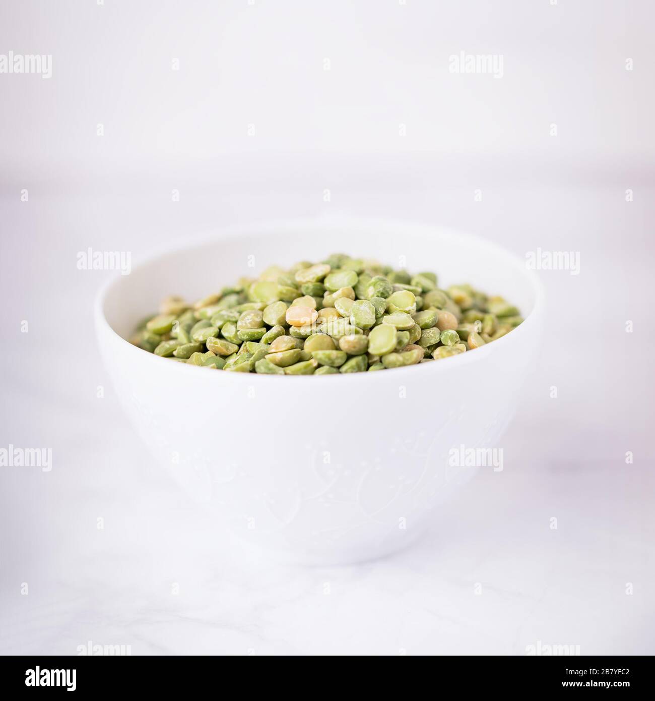 Trocken gespaltene hellgrüne Erbsen in einem weißen Becher Stockfoto