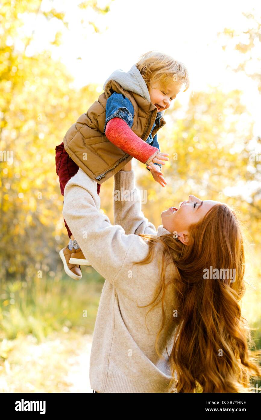 Lächelnde Frau hält ihren Sohn hoch im Wald Stockfoto