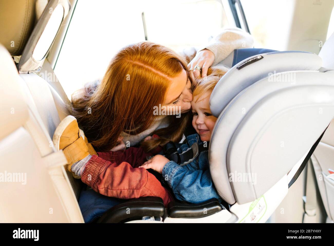 Frau küssen Sohn im Autositz Stockfoto