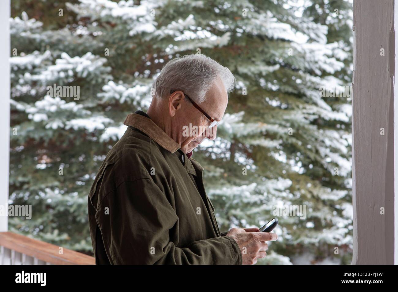 Älterer Mann, der Smartphone am verschneiten Baum benutzt Stockfoto