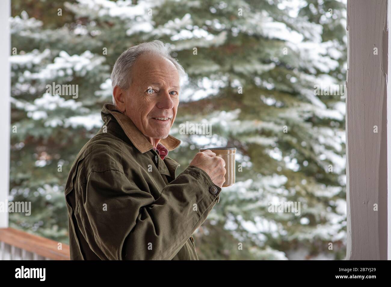Älterer Mann mit einer Tasse Kaffee von verschneiten Kiefern Stockfoto
