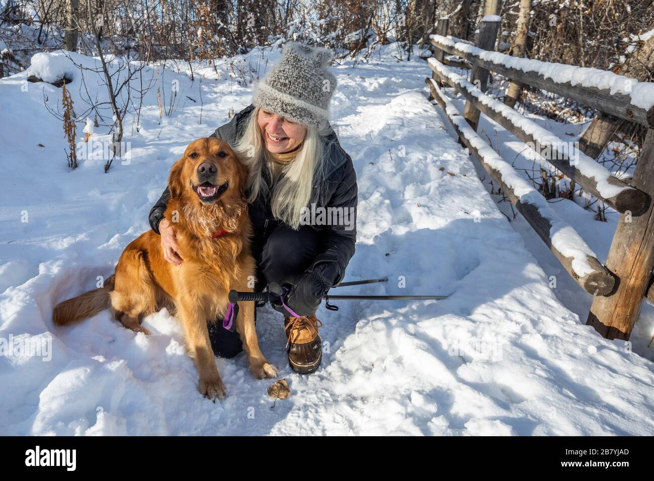 Lächelnde ältere Frau streichelt Hund im Schnee Stockfoto