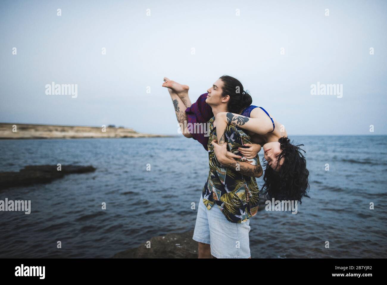 Junger Mann trägt Frau am Strand Stockfoto