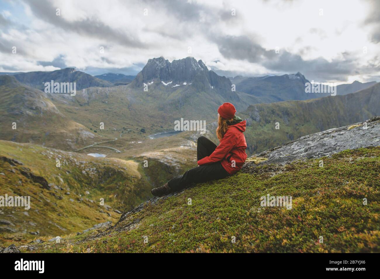 Junge Frau in roter Jacke sitzt auf dem Berg Stockfoto
