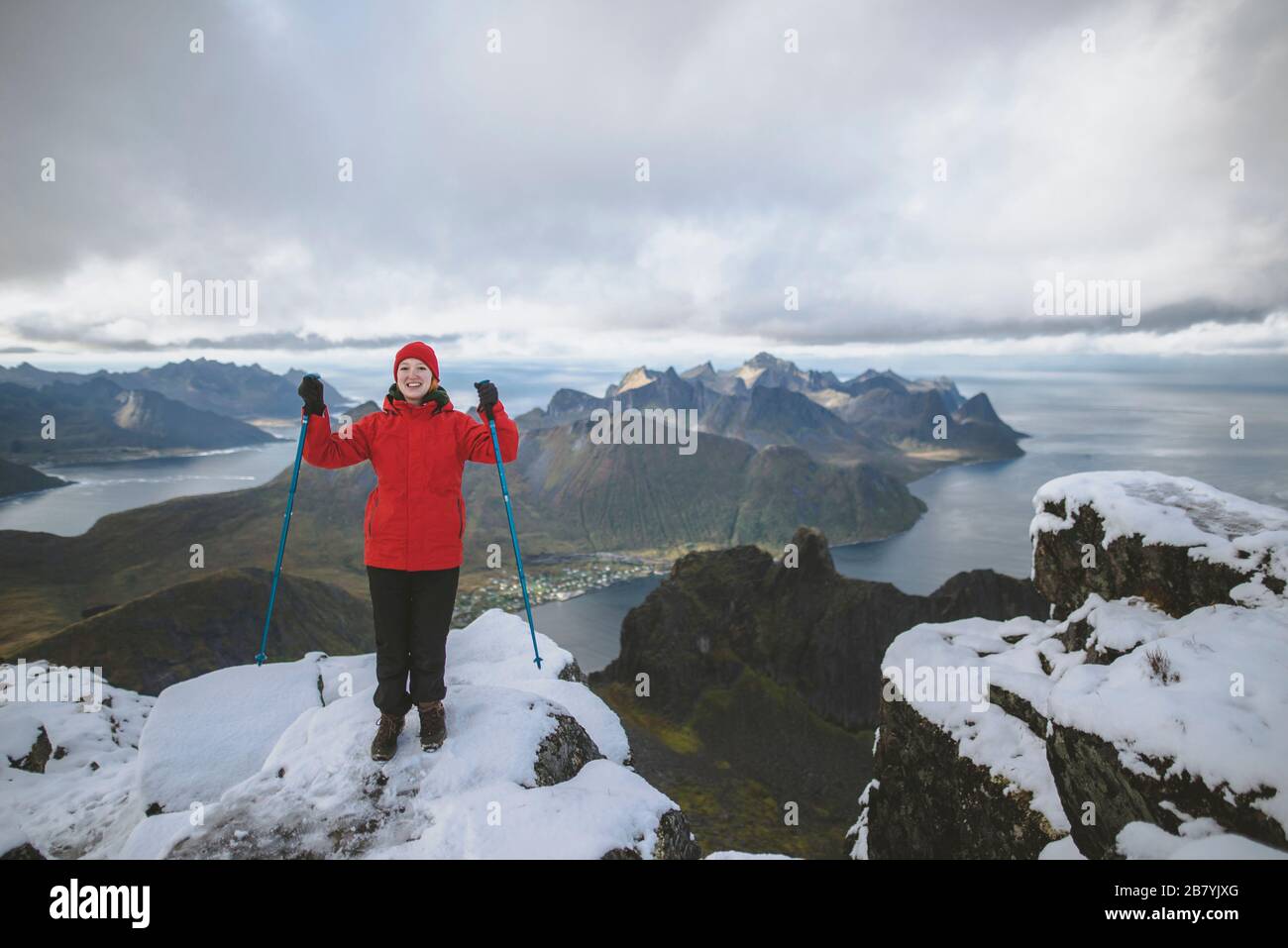 Junge Frau in roter Jacke mit Wanderstöcken auf verschneiten Berg Stockfoto