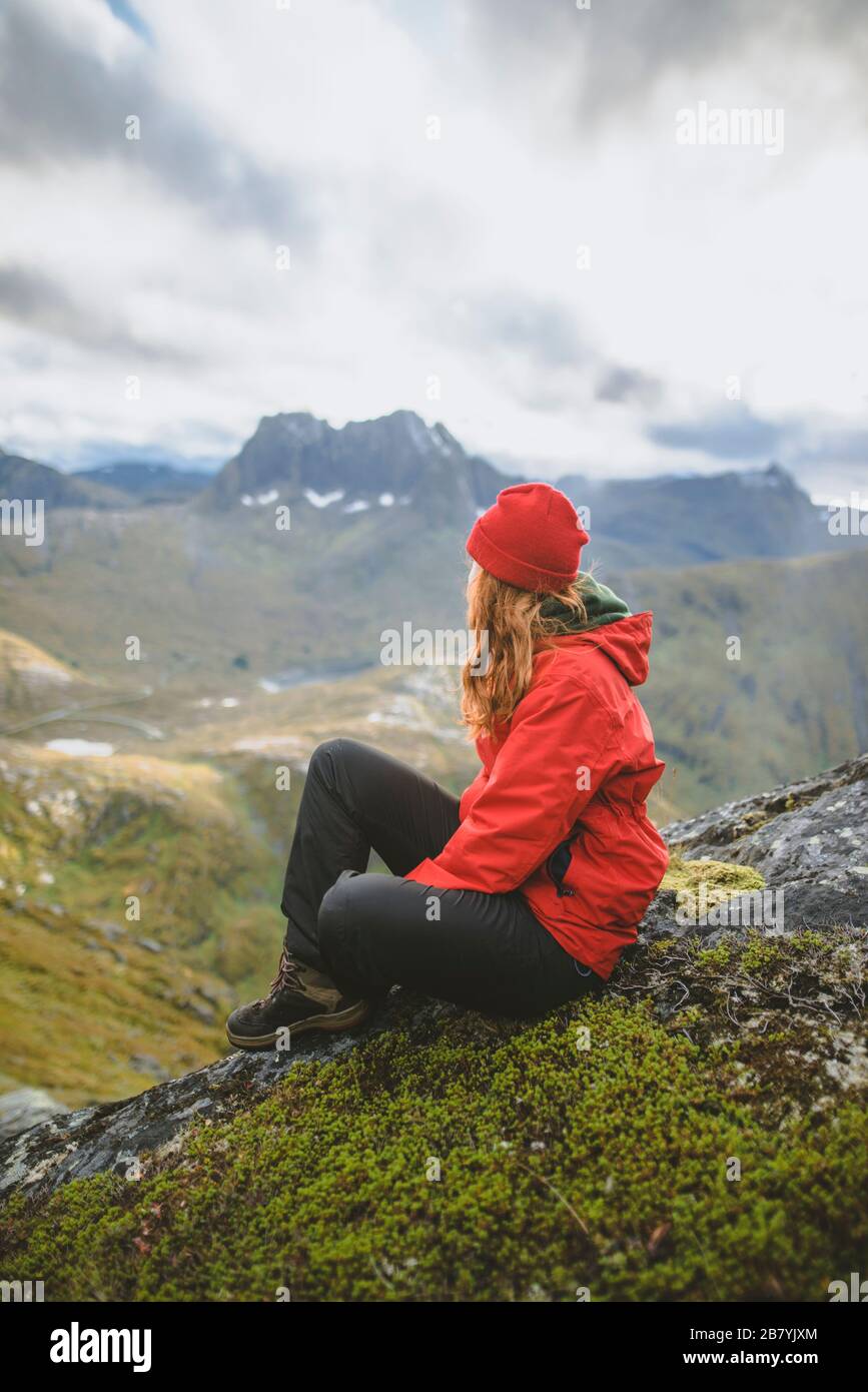 Junge Frau in roter Jacke sitzt auf dem Berg Stockfoto