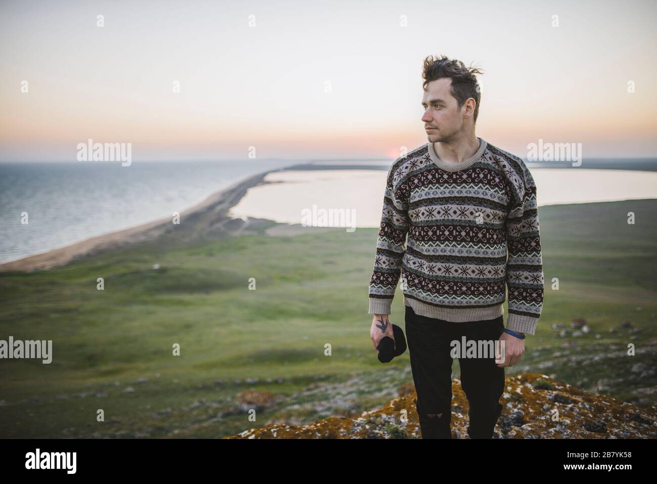 Junger Mann im gestreiften Pullover auf Hügel bei Sonnenuntergang Stockfoto