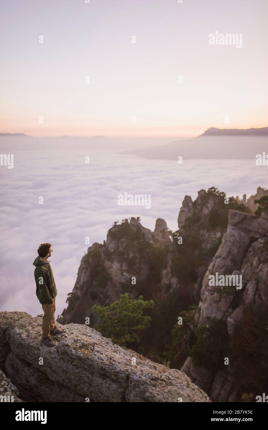 Junger Mann, der auf dem Berg über Nebel steht Stockfoto