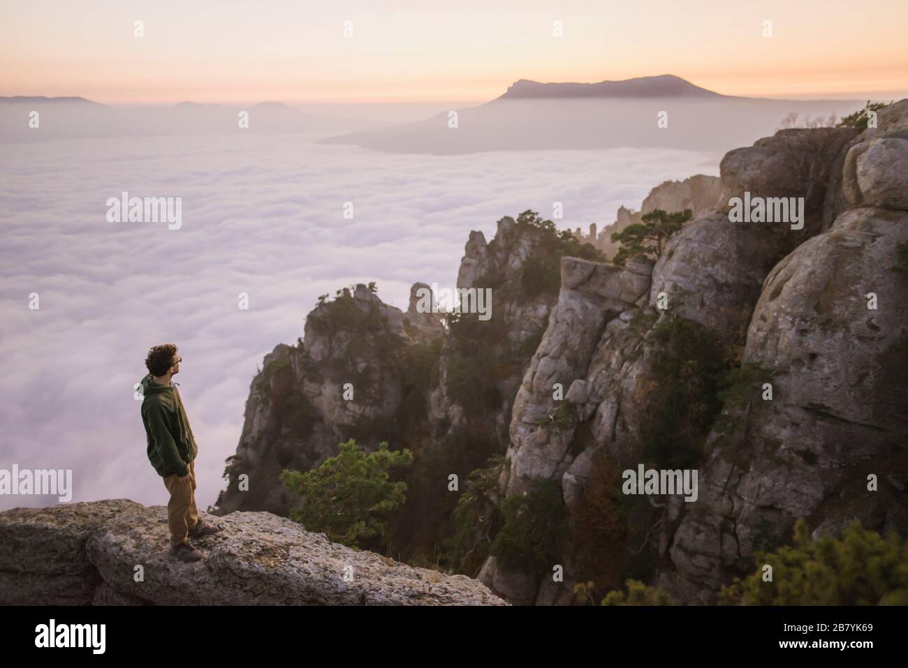 Junger Mann, der auf dem Berg über Nebel steht Stockfoto