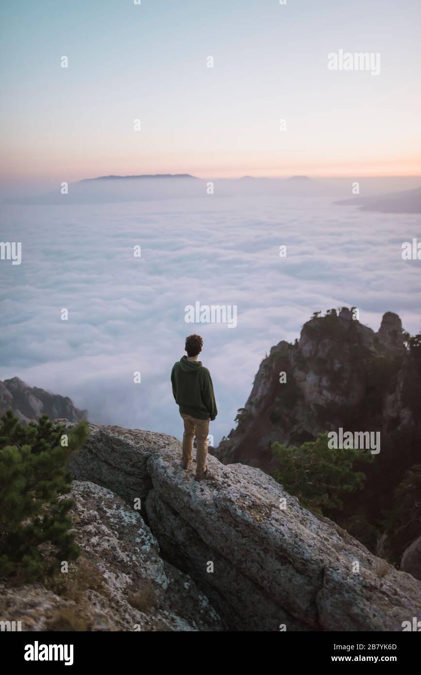 Junger Mann, der auf dem Berg über Nebel steht Stockfoto