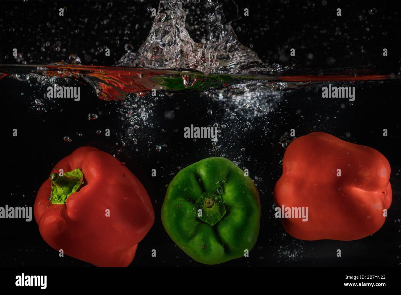 Paprika, die in Wasser fallen und Blasen im Aquarium erzeugen, schwarzer Hintergrund Stockfoto