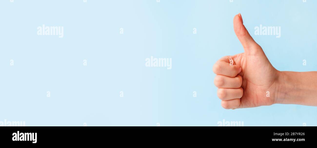 Nahaufnahme der weiblichen Hand mit Daumen nach oben Schild vor pastellblauem Hintergrund, Kopierraum, minimales Konzept Stockfoto