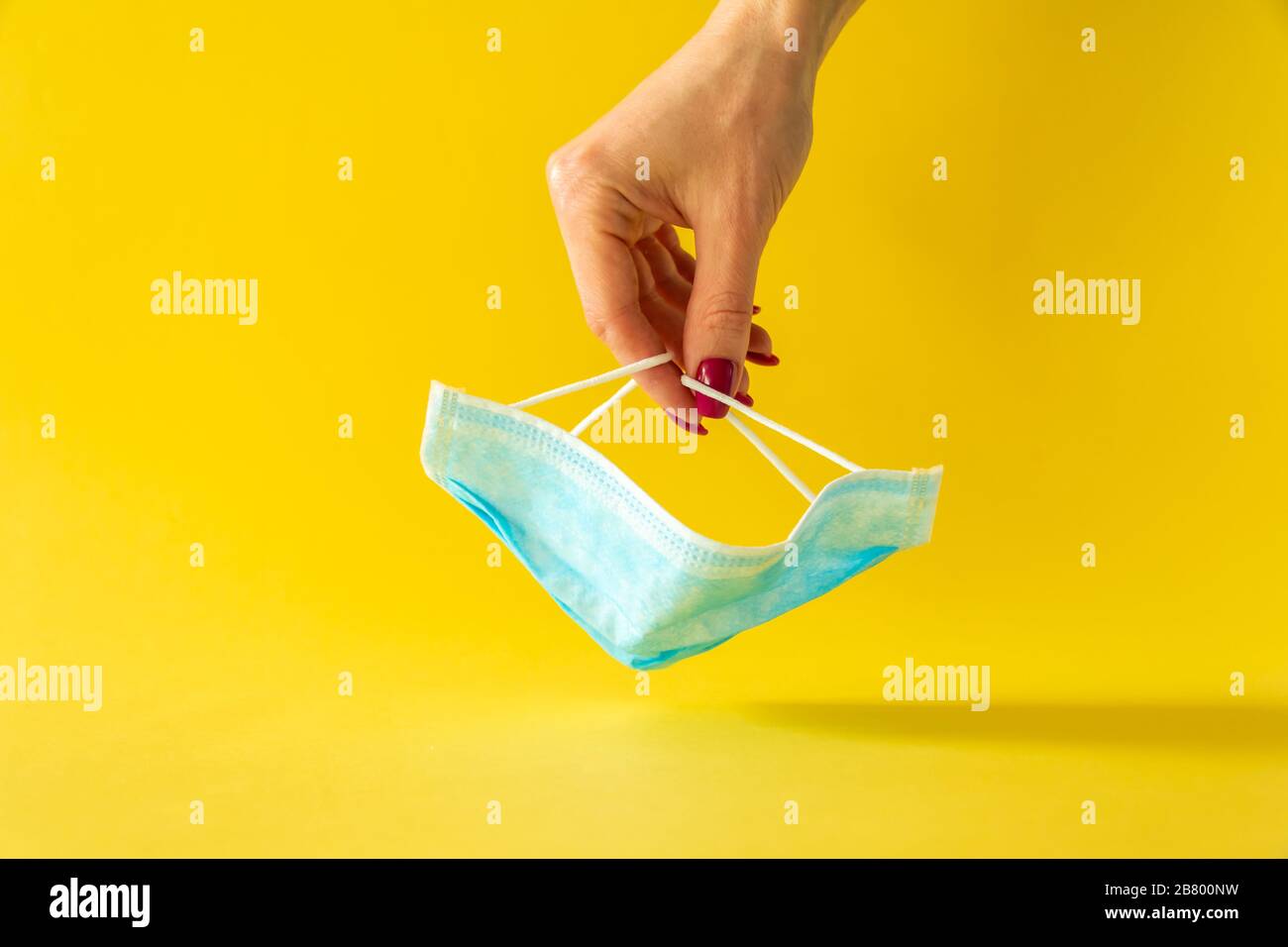 Verfahrensmaske. Operationsmaske mit Gummi-Ohrbändern auf gelbem Hintergrund mit Frauenhand. Stockfoto