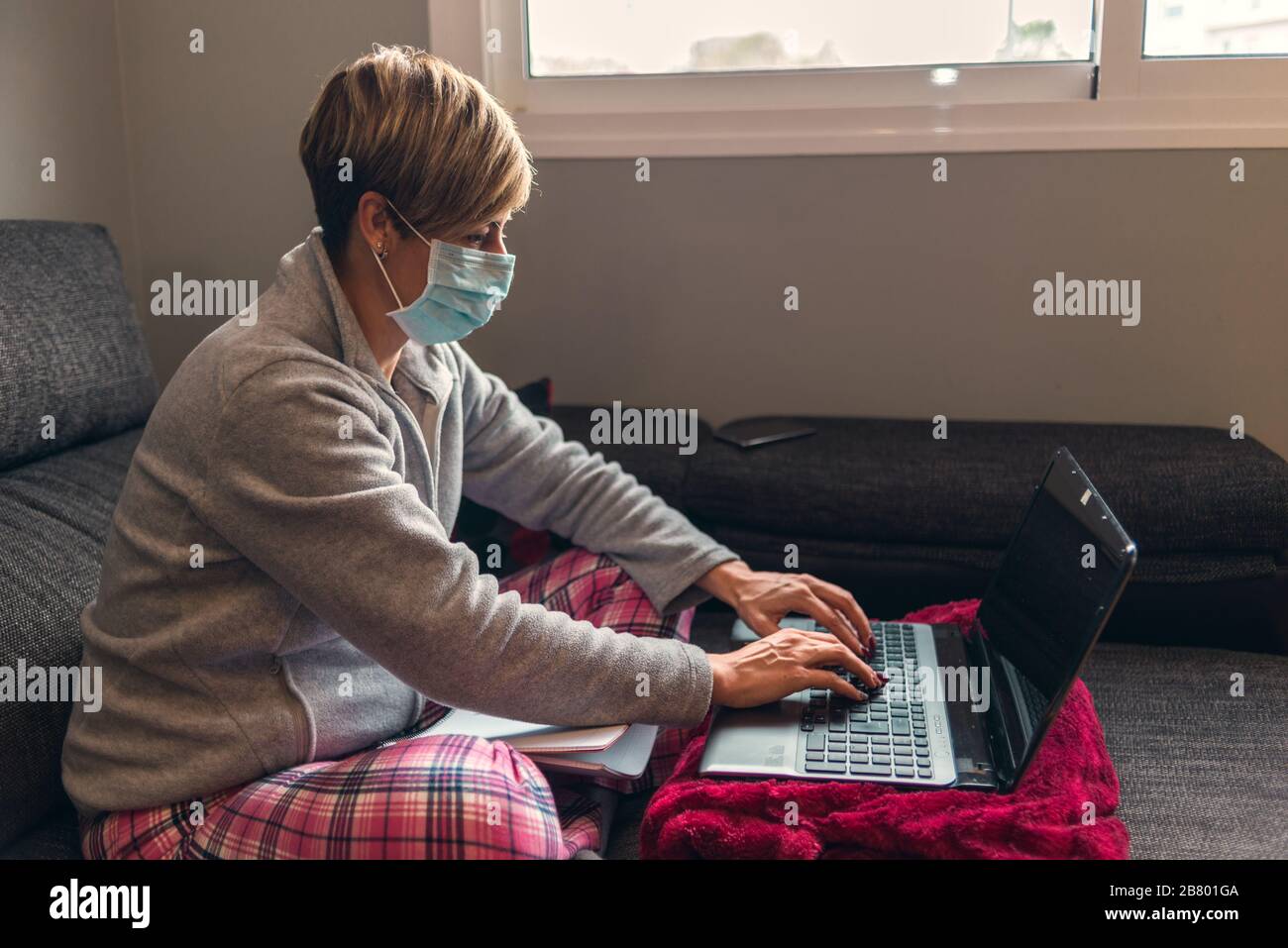 Konzept: Frau im freiwilligen Einschluss mit Pyjama und chirurgischer Maske zur Vorbeugung von Coronavirus Kovid19-Virus. Sie arbeitet zu Hause mit dem Sofa a Stockfoto