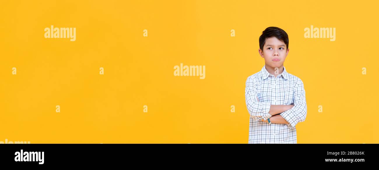 Sulky gelangweilter Junge, der Mund pfenund mit Arm gekreuzte Geste dachte, isolierte gelben Bannerhintergrund Stockfoto