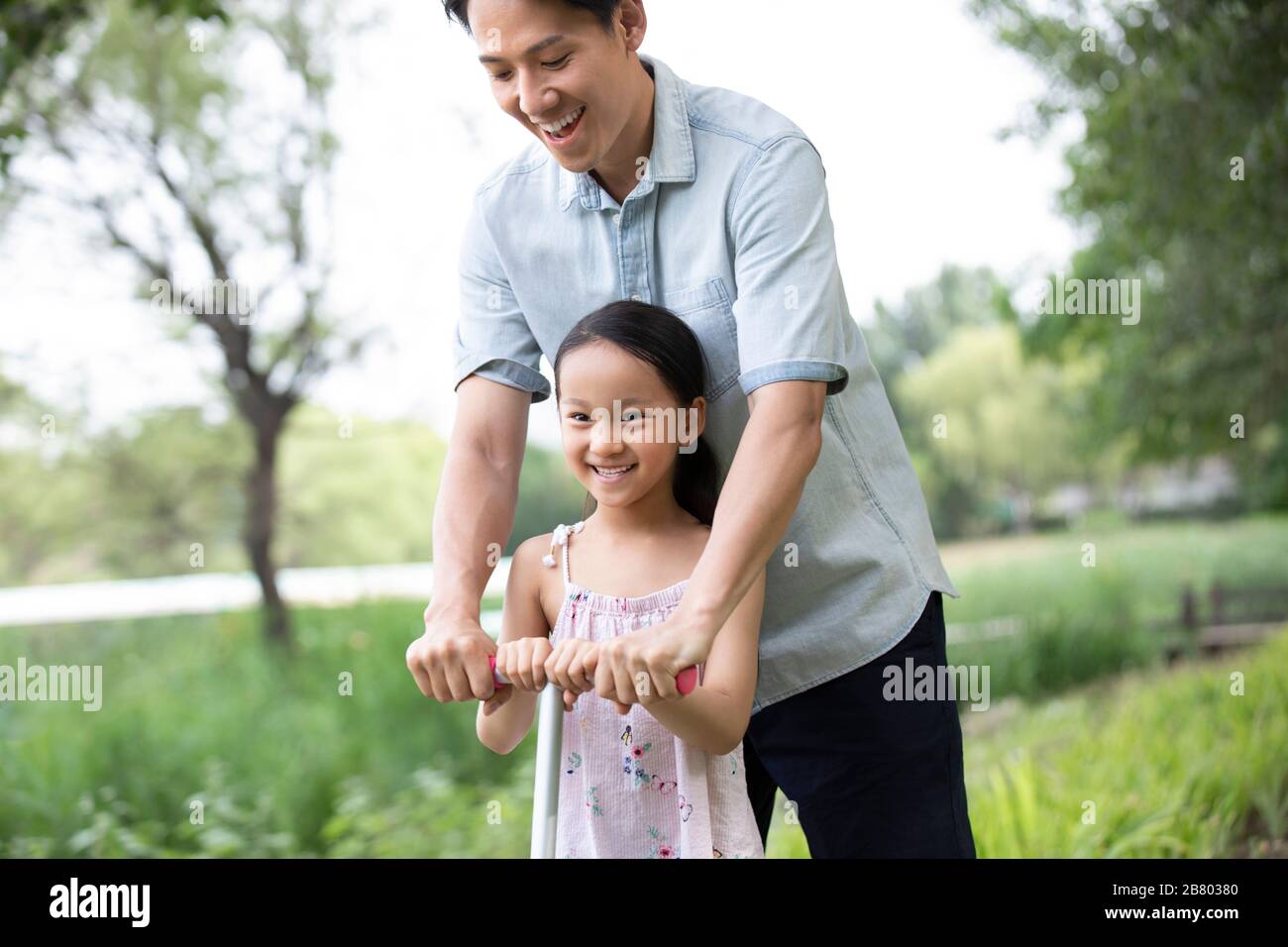 Glücklicher chinesischer Vater und Tochter, die im Park mit einem Push-Roller fahren Stockfoto