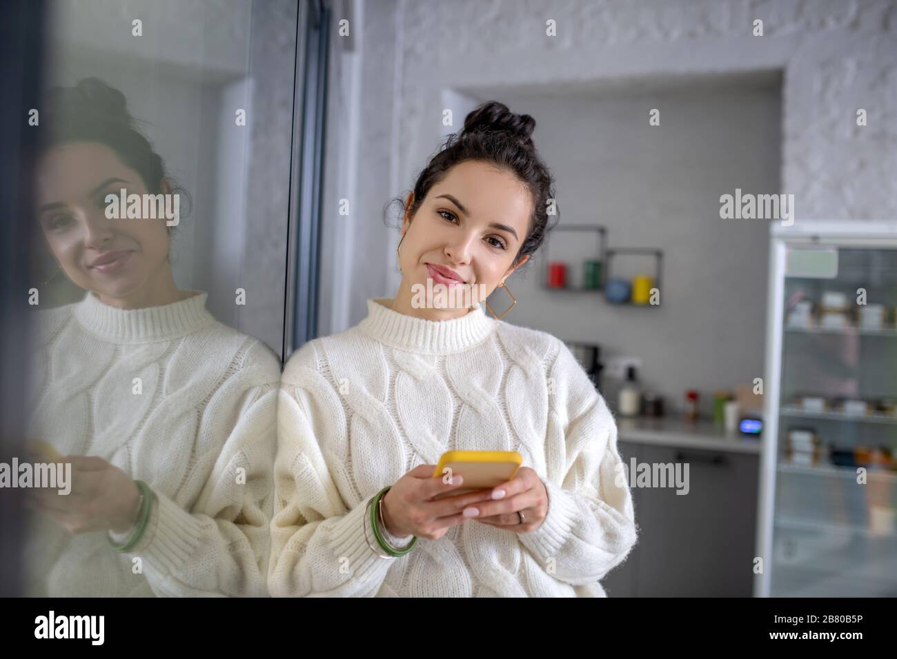 Junge Frau lehnt sich an die Glaswand und hält Handy Stockfoto