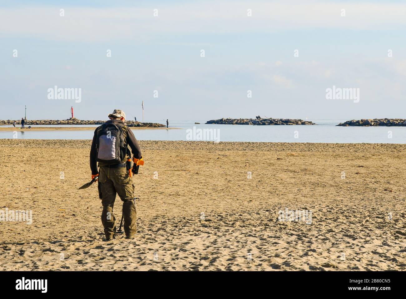 Ein Mann von hinten auf der Suche nach verborgenen schätzen mit einem Metalldetektor am Strand von Arma di Taggia, Imperia, Ligurien, Italien Stockfoto