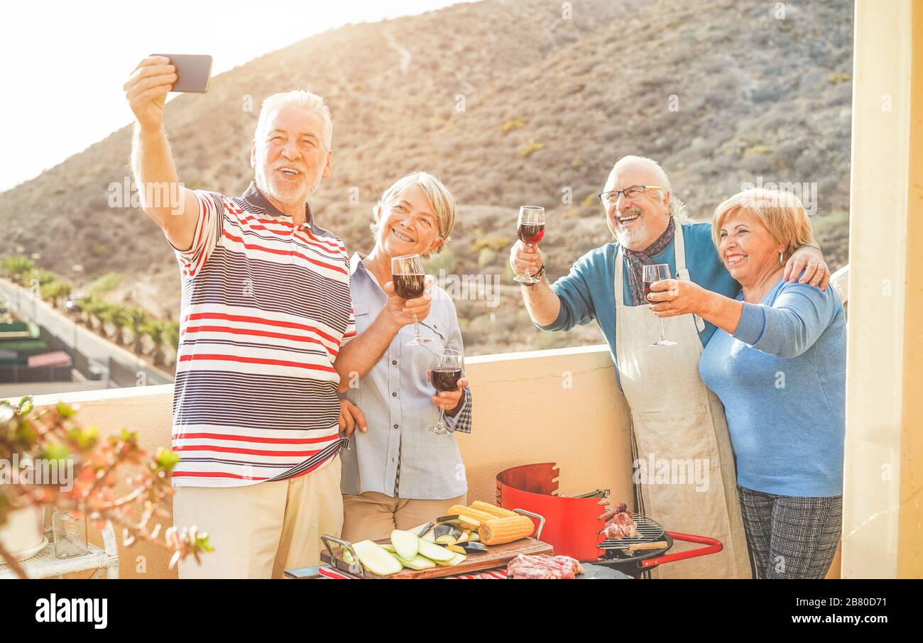 Fröhliche Senioren Freunde, die mit einer Smartphone-Kamera beim Grillabendessen auf der Hausterrasse eine selfie machen - reife Leute, die mit neuer Trendtechnologie Spaß haben Stockfoto