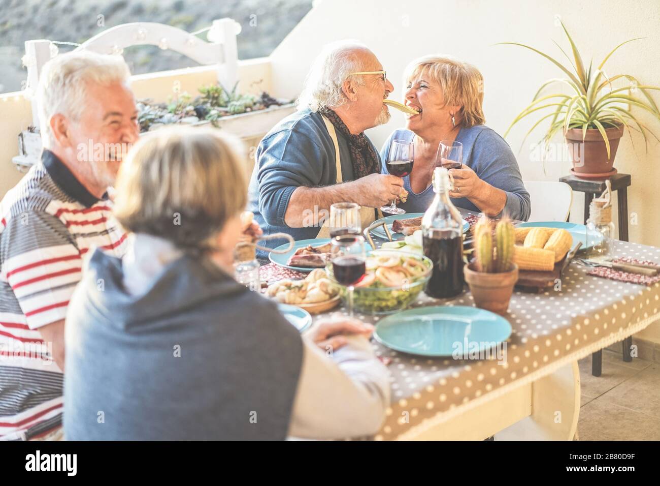 Älteres Paar mit Spaß beim Barbecue-Dinner auf der heimischen Terrasse - Rentnerfreunde, die Sommerferien genießen und Wein trinken - konzentrieren Sie sich auf den richtigen Peo Stockfoto