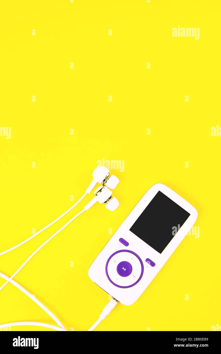 Weißer Musik-Player mit Ohrhörern auf gelbem Hintergrund. Vertikal, Kopierbereich, flaches Layout. Stockfoto