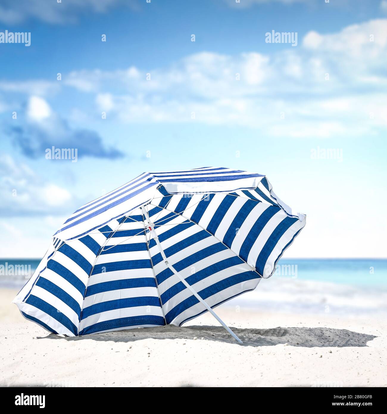 Blau-weißer Regenschirm am Strand. Freie Platz für Ihre Dekoration. Sommerlicher sonniger Tag. Blauer Himmel und Ozeanlandschaft. Hintergrund der Sommerzeit. Stockfoto