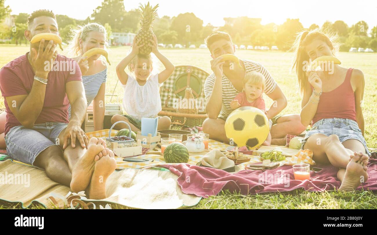 Fröhliche Familienfreunde, die mit Früchten spielen und am Wochenende lustige Gesichter beim Picknick im Freien machen - Eltern haben Spaß beim Essen und Lachen ihrer Kinder Stockfoto
