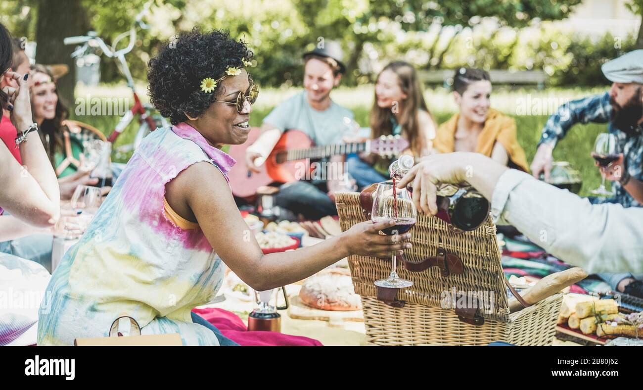 Eine Gruppe von Freunden, die Picknickmittagung machen und Wein im Freien trinken - junge Leute haben Spaß beim Essen und Entspannen - konzentrieren sich auf das gesicht afrikanischer Mädchen - out Stockfoto