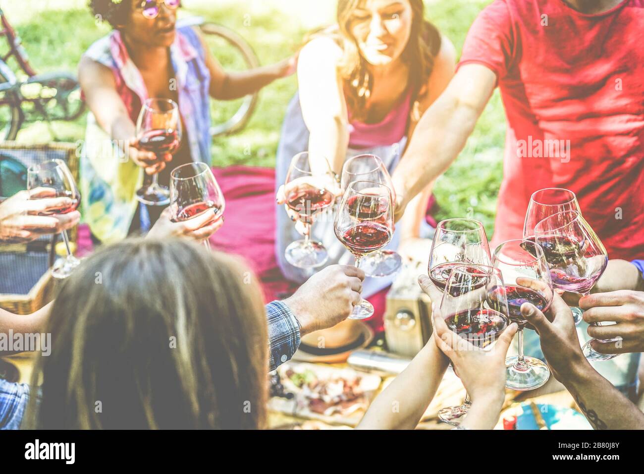 Eine Gruppe von Freunden, die ein Picknick genießen, während sie mit Rotwein jubeln und im Freien Imbiss-Vorspeisen essen - junge Leute trinken und Spaß haben Stockfoto