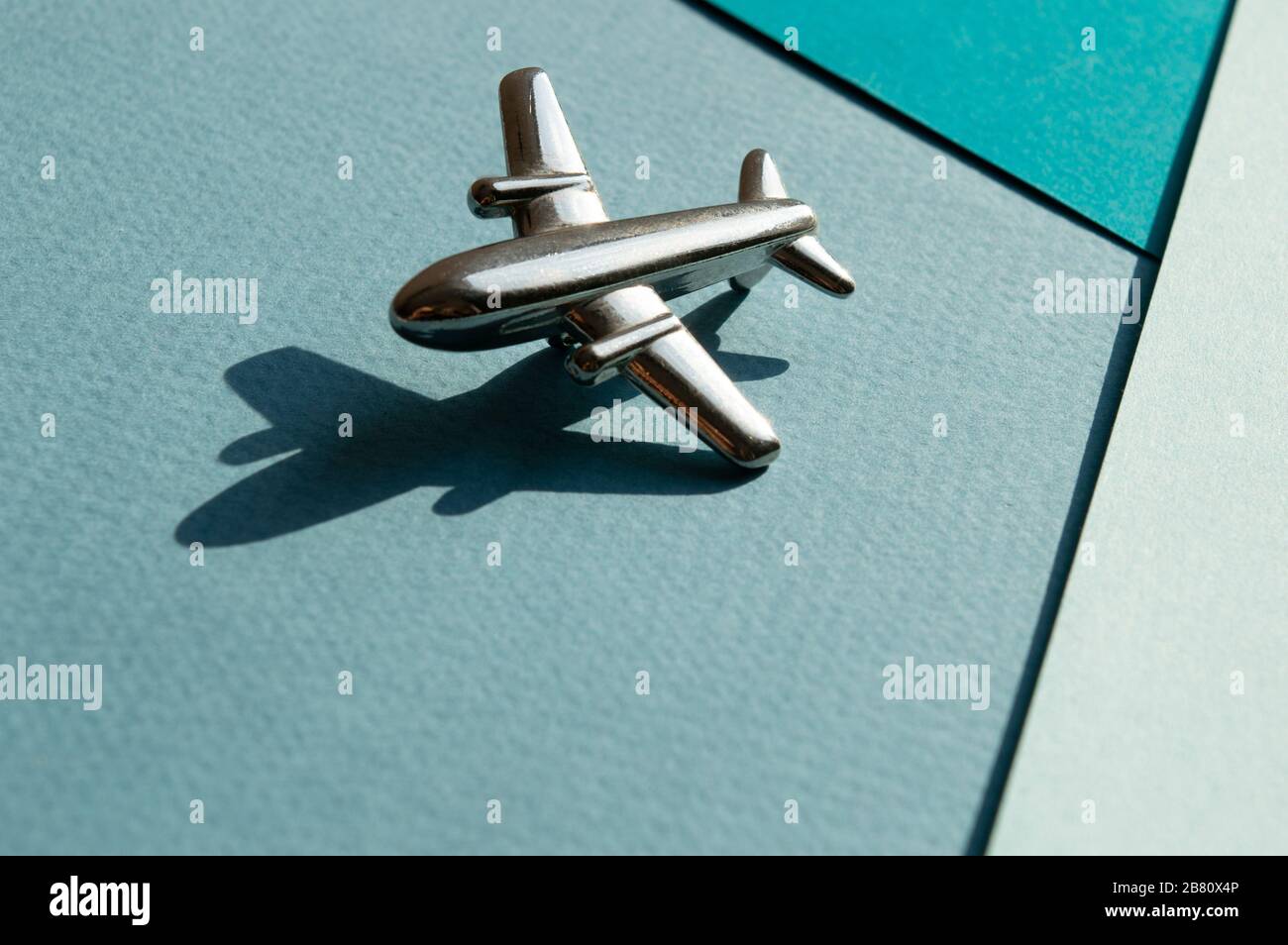 Metallfigur des kleinen Flugzeugs mit Schatten auf Turqouise und hellblauem Geometriehintergrund. Flatlay, Draufsicht, Layout. Luftfahrtindustrie Stockfoto