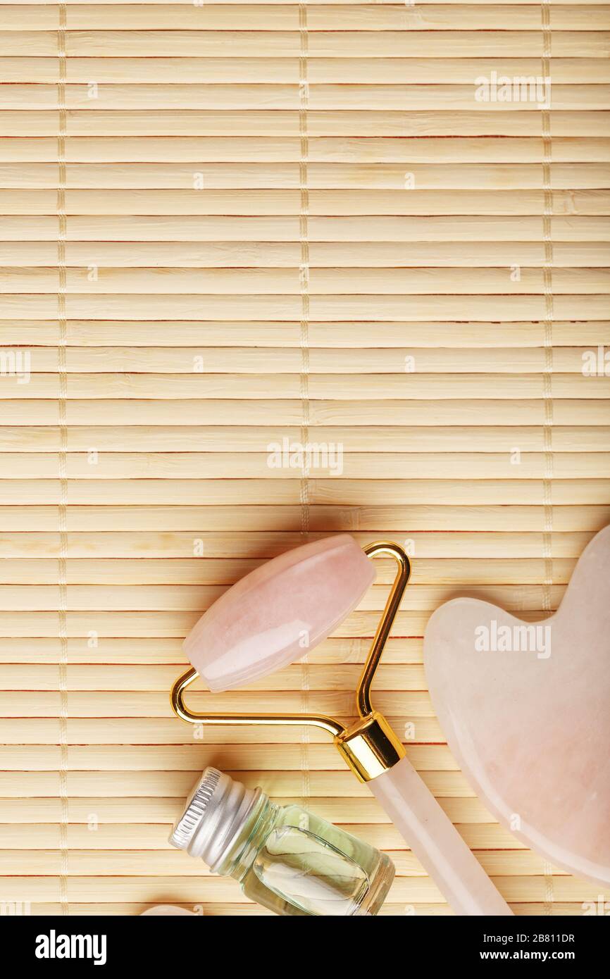 Gua sha-Massage aus natürlichem Rosen-Quarz-Roller, Jadestein und Öl, auf Bambushintergrund für Gesichts- und Körperpflege. Stockfoto